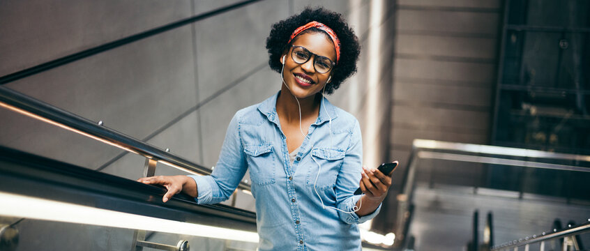 Smiling young woman riding up an escalator listening to music