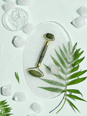 Self made moisturizer and green jade face roller on oval piece of ice and ice cubes. Exotic palm...