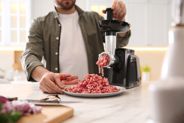 Man using modern meat grinder in kitchen, closeup