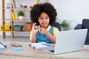 African american girl counting on fingers near laptop and stationery on table