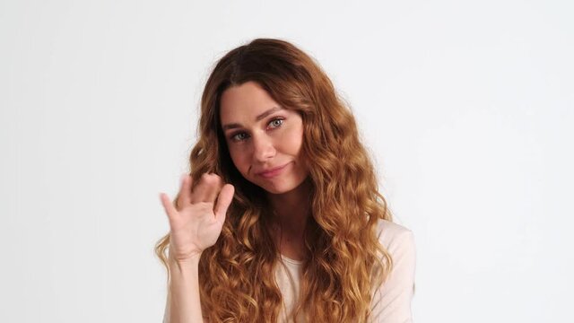 A displeased woman is doing blablabla gesture while shaking her hand showing nonsense content standing isolated over a white wall in the studio