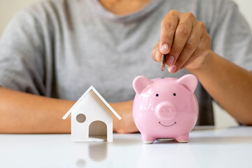 The girl put the money in the piggy bank and the house model. financial concept Mortgage and Real Estate Mortgage