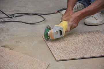 man hand cutting a tile using an angle grinder on the floor at construction site