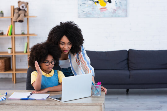 African American Kid Raising Hand Near Laptop And Mother At Home