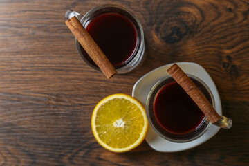 Mulled wine in glass cups with cinnamon and oranges on a wooden table.