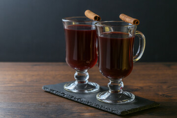 Mulled wine in glass cups with cinnamon and oranges on a wooden table.