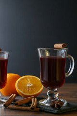 Mulled wine in glass cups with cinnamon and oranges on a wooden table.
