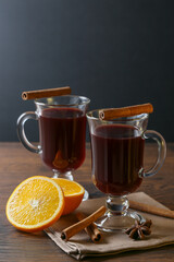 Mulled wine in glass cups with cinnamon and oranges on a wooden table.
