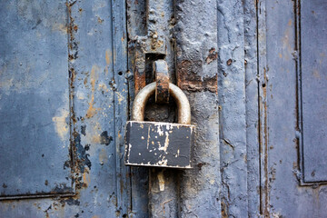 A blue old wooden door with a rusty steel lock. Farm gate from planks with an old padlock. The lock on the door of the shed. Reliable old barn rusty padlock on a wooden door 