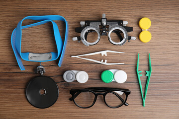 Different ophthalmologist tools on wooden background, flat lay