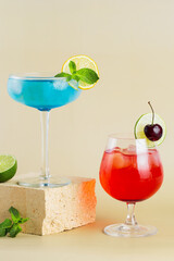 two glasses of cocktails. Blue Lagoon cocktail with lime and cocktail with grenadine on modern still life on podium on beige background. Festive party. Summer holiday mocktail. Vertical