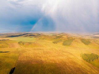 Naklejka na ściany i meble Fields of autumn grass, mountains and hills lit by the evening sun, rare trees and the sky in clouds, it is raining and a rainbow. Khakassia