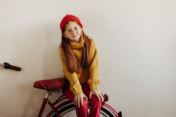 Wonderful girl with freckles and ginger hair in red cap, bright yellow sweater and pants looking...