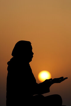 Silhouette of a Muslim woman in abaya praying with her hands at sunset, United Arab Emirates