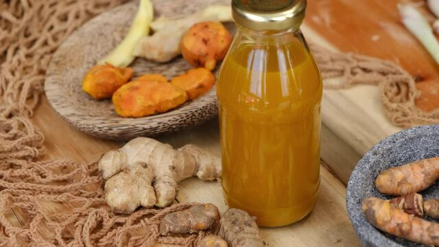 Bottle of Jamu drink- Indonesian herbal beverage with natural ingredients: turmeric, ginger, lime, palm sugar, lemongrass, tamarind on wooden table. Healthy lifestyle