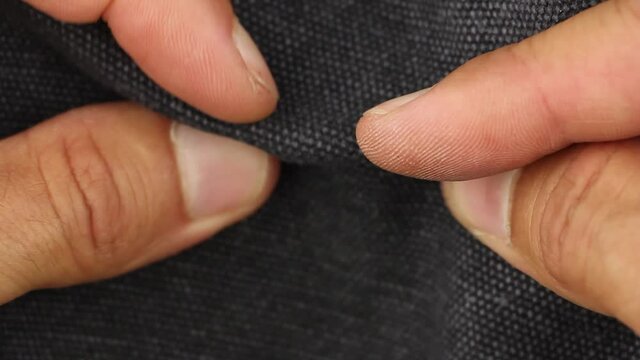 human hand tests, rumples and crumples black tarpaulin fabric textile material, close-up view