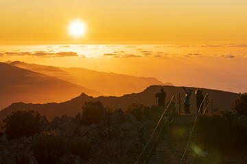 Tourists photographing sunset with smartphone from Pico Ruivo mountain peak, Madeira, Portugal