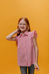 Optimistic joyful redhead little girl in jeans and red striped shirt smiles. Cool child ok great mood poses on orange background.