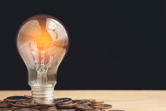 Warm light bulb on pile of coins, look like warming, saving  energy on wooden table isolated on black background.