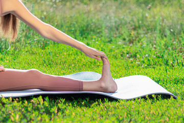 The girl is engaged in yoga in nature very close-up. A woman in the park doing stretching while sitting on green grass on a blurred background. Concept illustration of outdoor sports.