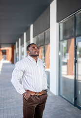 Fototapeta premium Black businessman in white shirt standing on a street. Confident office manager holding on modern urban street.