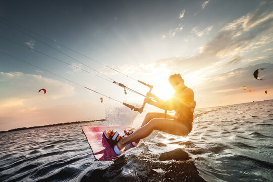 Professional kite surfer woman rides on a board with a plank in her hands on a leman lake with sea water at sunset. Water splashes and sun glare. Water sports