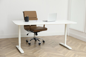 Stylish workplace with laptop and comfortable armchair near white wall indoors. Interior design