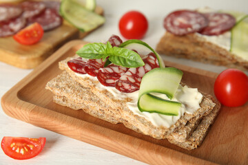 Fototapeta na wymiar Fresh rye crispbreads with salami, cream cheese and cucumber on white wooden table, closeup