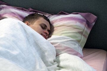 The young man sleeps on the bed under the covers. Comfortable and cozy sleeping environment. Horizontal photo.