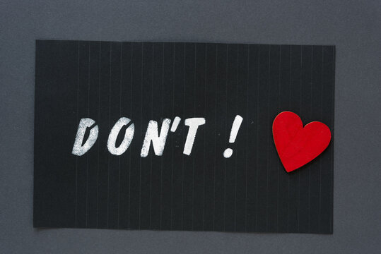 the word "don't" in alpha/numeric plastic stencil letter type - hand painted in white acrylic paint - on black pad paper with faint lines and red heart - on dark gray paper