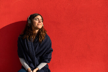 Young caucasian woman with headphones listens to music with smiley positive face. isolated on red background.