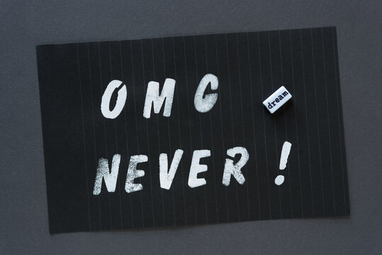 the words "OMG never" in alpha/numeric plastic stencil letter type - hand painted in white acrylic paint - on black pad paper with faint lines and the word bead "dream" - on dark gray paper
