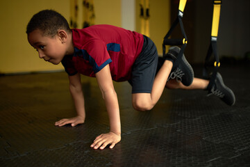 Naklejka premium Latino american kid performing difficult exercise on machine in gym. Train strength and endurance from childhood. Sport, hobby, exercise, gymnast, health, training, athlete concept