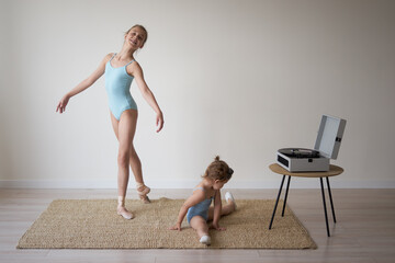 Fototapeta na wymiar an adult ballerina girl shows the movements of a little girl to a child who is sitting on the floor and learning