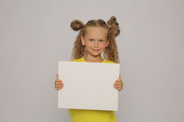 a beautiful happy blonde girl with ponytails in a yellow T-shirt horizontal photo holds a white sheet in her hands and points at it with her finger