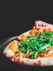 woman Hand takes a slice of Pepperoni Pizza with Mozzarella cheese, salami, Tomatoes, pepper, Spices and Fresh arugula in cafe