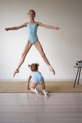  two girls the older ballerina in a jump the younger one crawls on her knees in the hall under the...