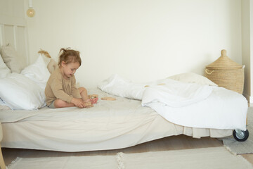 a little girl in light pajamas is sitting in a bright bedroom in the morning and playing with wooden eco toys