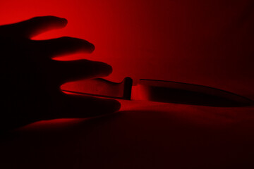 Silhouetted hand reaching for knife bathed in red light