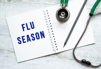 FLU SEASON is written in a notebook on a wooden table next to stethoscope.