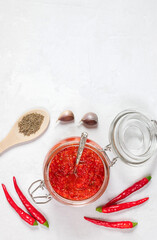 Adjika with a jar on a white background. Hot chili pepper sauce paste harissa. Vertical orientation. Copy space, top view, flat lay.