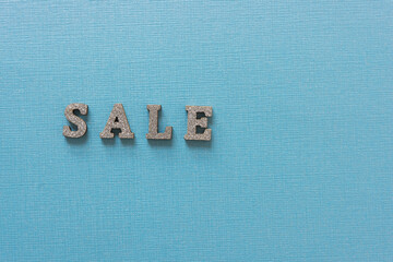 the word "sale" in silver glitter wooden letters on a light blue metallic paper background
