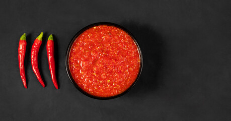 Adjika on a black background. Hot chili peppers harissa sauce. Homemade rose harissa in a bowl....