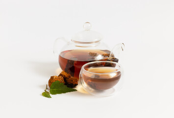 Chaga drink. Infusion with chaga mushroom in a glass teapot and cup on a white background.