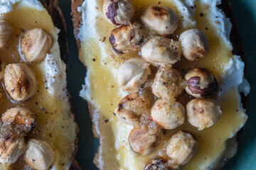 Two bread toast with cream cheese, roasted hazelnuts, honey, pepper and salt, close up, top view