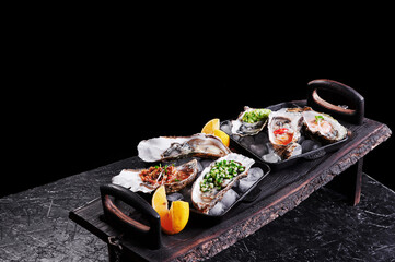 Assorted fresh open oysters in a plate with ice and lemon on a black texture background, top view. High quality photo