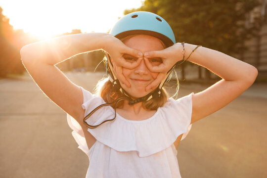 Funny young rollerblader girl making glasses sign with her hands, laughing cheerfully