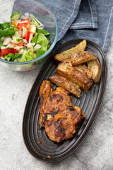 Minted lamb chop on a black dish with rosemary covered potato wedges and salad