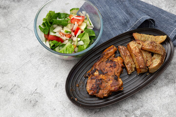 Minted lamb chop on a black dish with rosemary covered potato wedges and salad