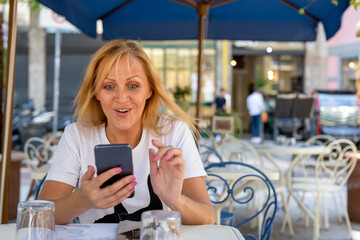 adult caucasian woman looking at her smart phone with surprise, female person holding cellphone and using it, copy space